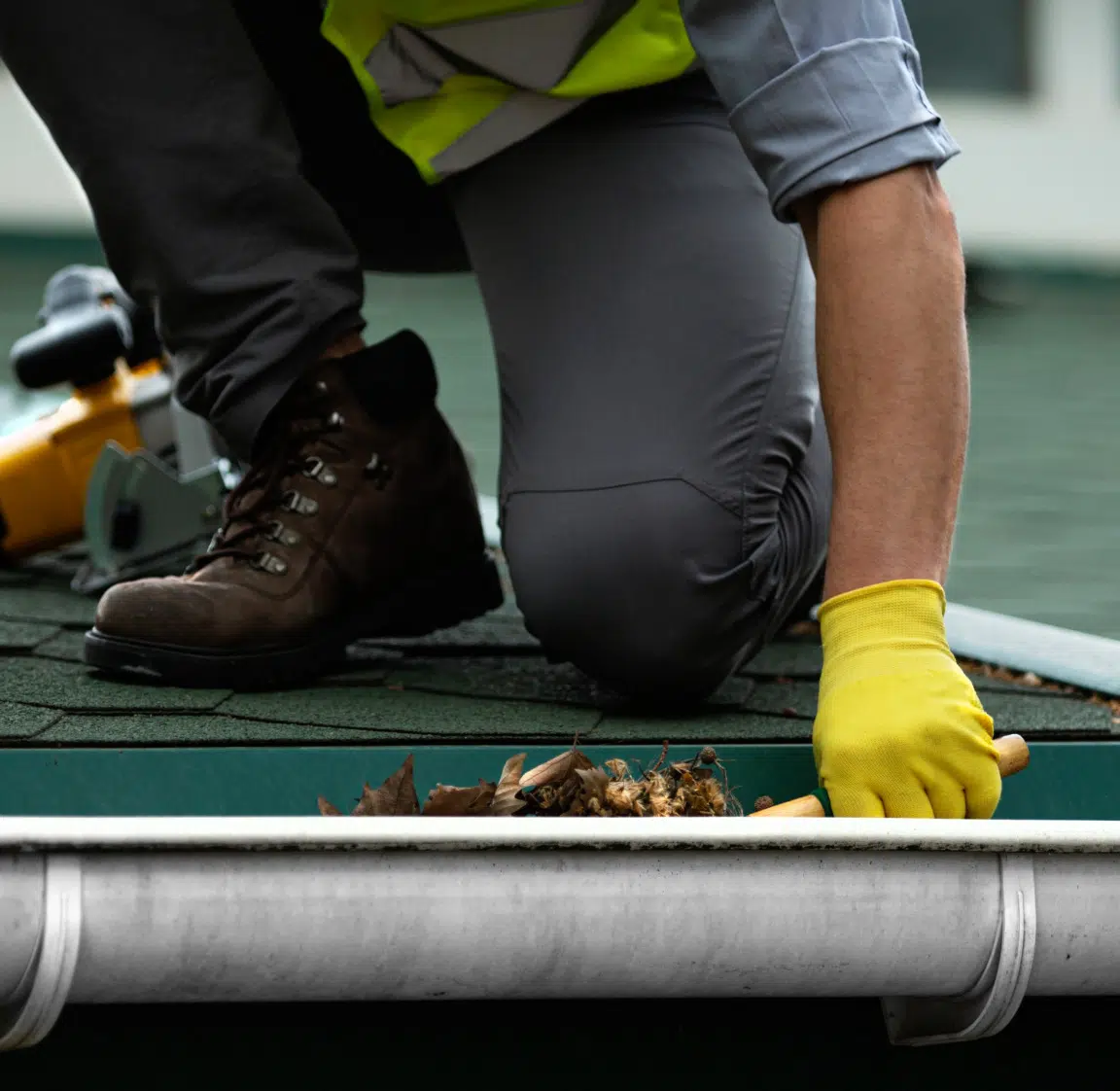 Technicien en nettoyage de gouttière sur une toiture nettoyant la gouttière